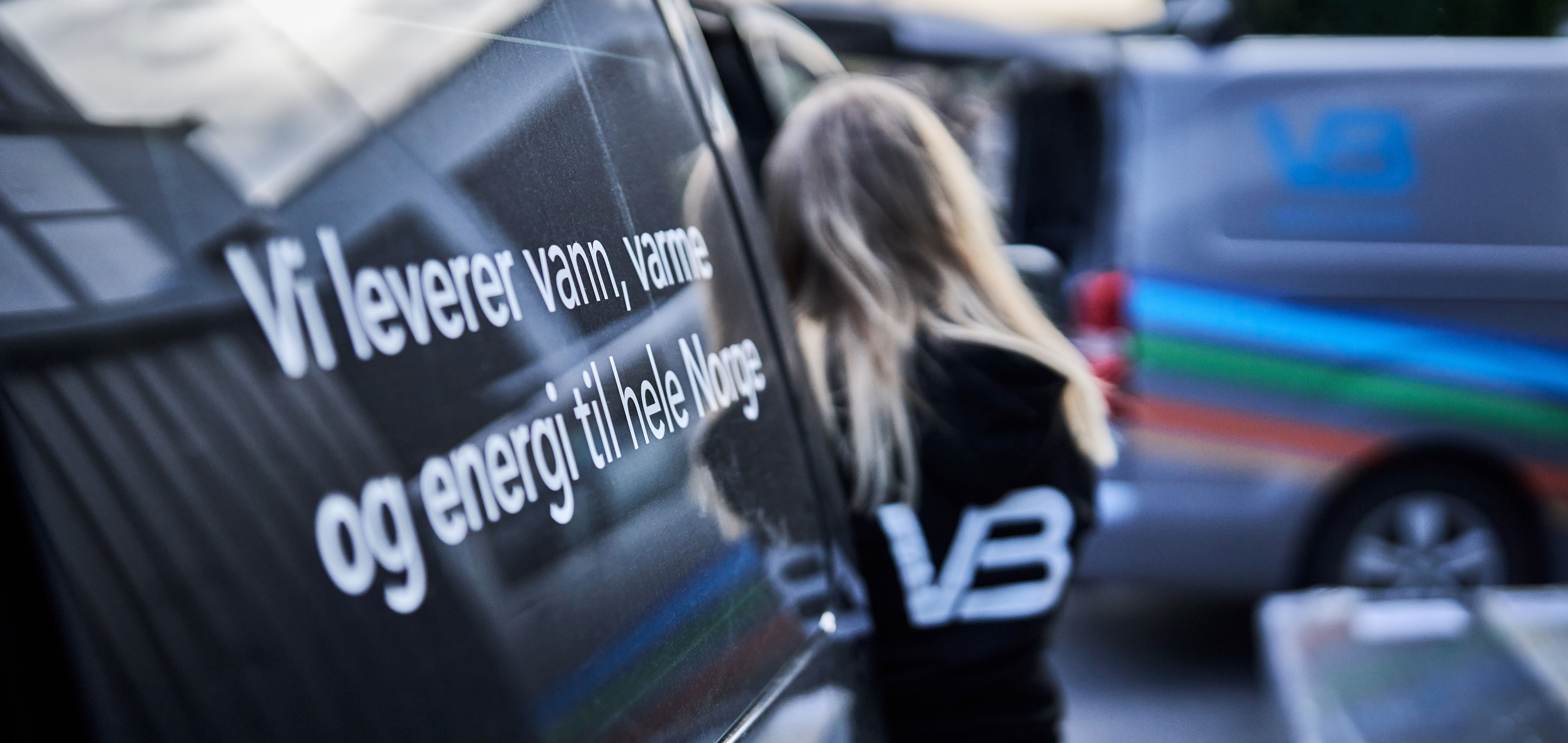 VB-rørlegger med ryggen til utenfor firmabil med tekst på siden av bilden: "Vi leverer vann, varme og energi til hele Norge"